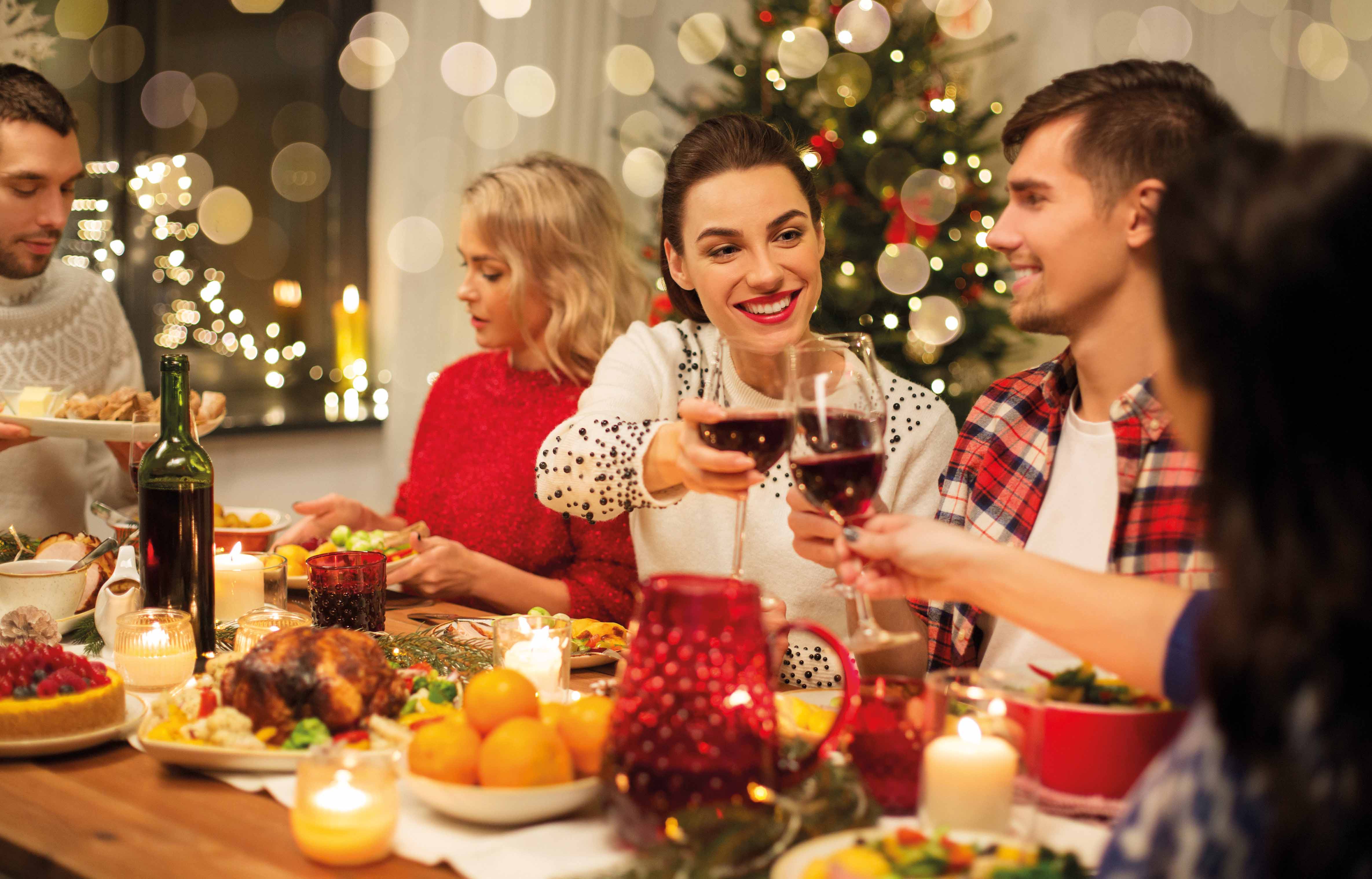 holidays and celebration concept - happy friends having christmas dinner at home, drinking red wine and clinking glasses