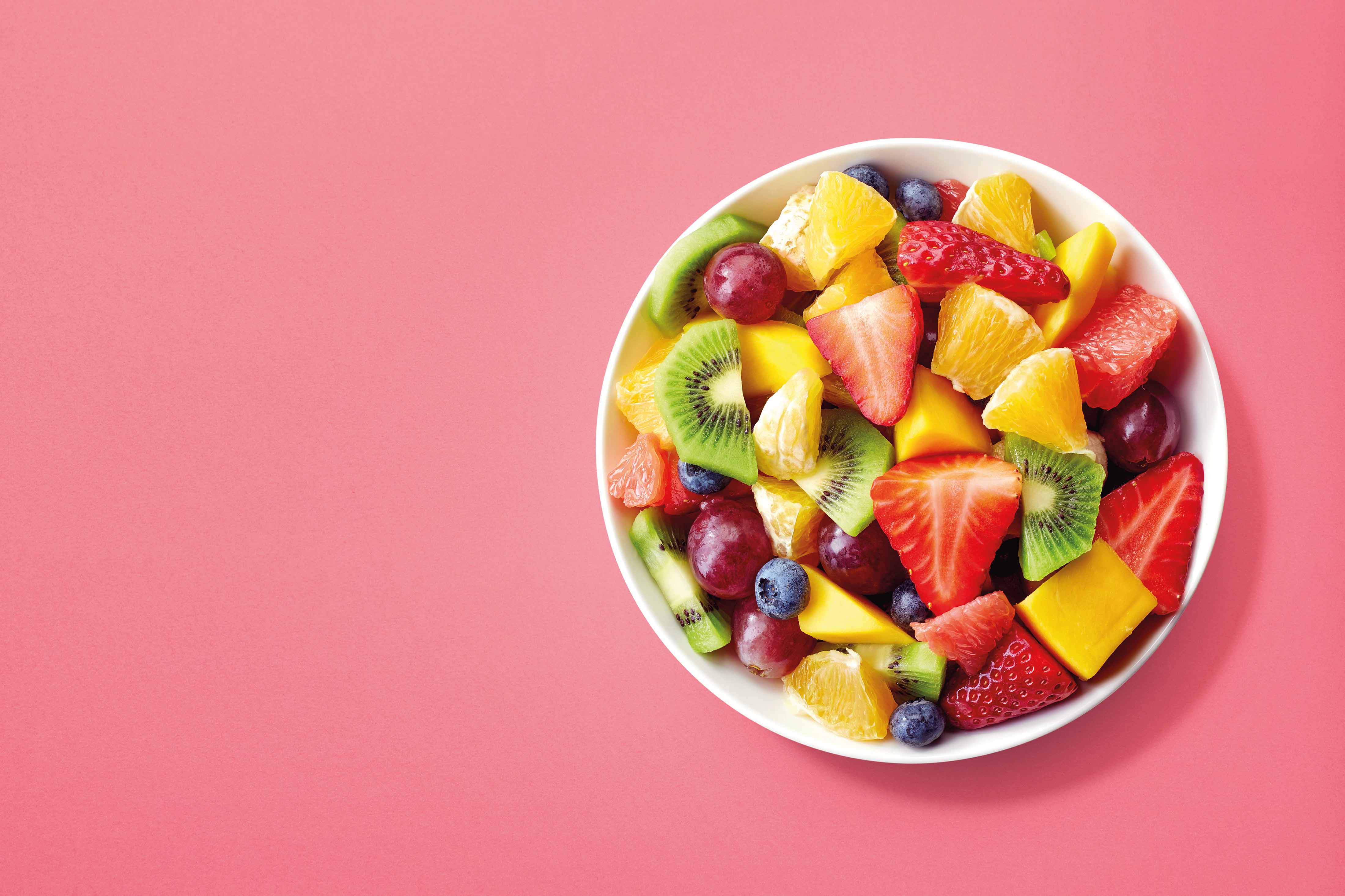 Bowl of healthy fresh fruit salad on pink background, top view