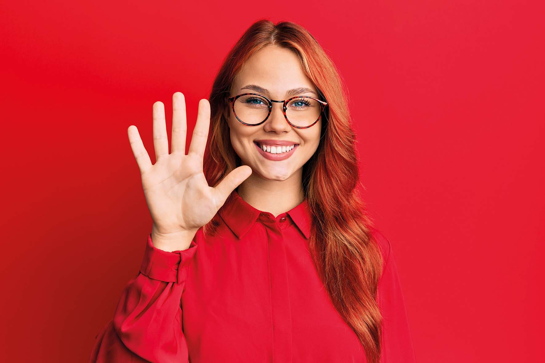 Young beautiful redhead woman wearing casual clothes and glasses over red background showing and pointing up with fingers number five while smiling confident and happy. 